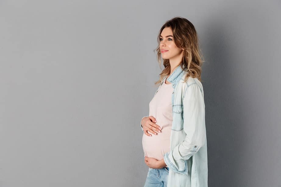 אישה צעירה בהריון מחזיקה את הבטן ונשענת על הקיר
