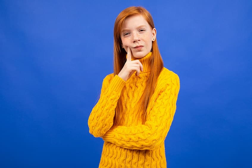 בחורה עם סוודר צהוב עושה פרצוף חושב ומסוקרן