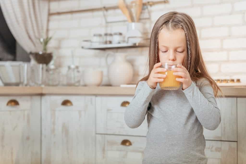 ילדה עם מחלת הפה והגפיים שומרת שותה מיץ תפוזים במטבח