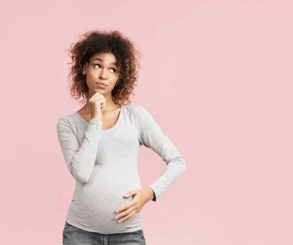 בחורה בהריון בחולצה אפורה חושבת רקע ורוד